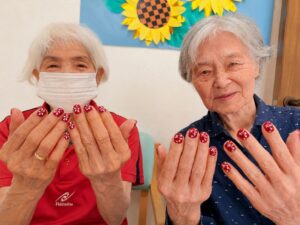お二人:赤いお花模様のネイルを見せるご利用者様 高齢者のネイル ファミリーケア心の家 上池台